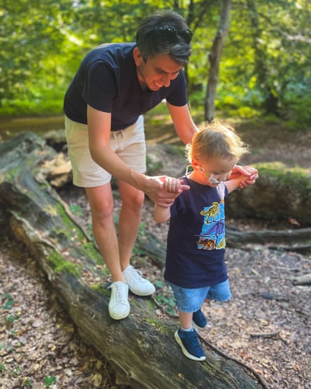 Graham Tatham holding his three-year-old son’s hands while walking in woods