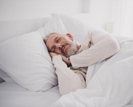 Middle-aged man with beard asleep with white bed linen and wearing white top