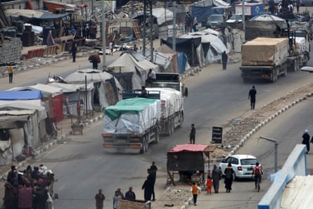 Humanitarian aid trucks drive past tents used as temporary shelters by displaced Palestinians