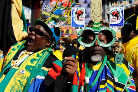 Two South Africa fans successful squad shirts and scarves, 1 wearing a home-made chapeau and 1 wearing home-made glasses, cheer for their squad astatine nan 2010 World Cup.