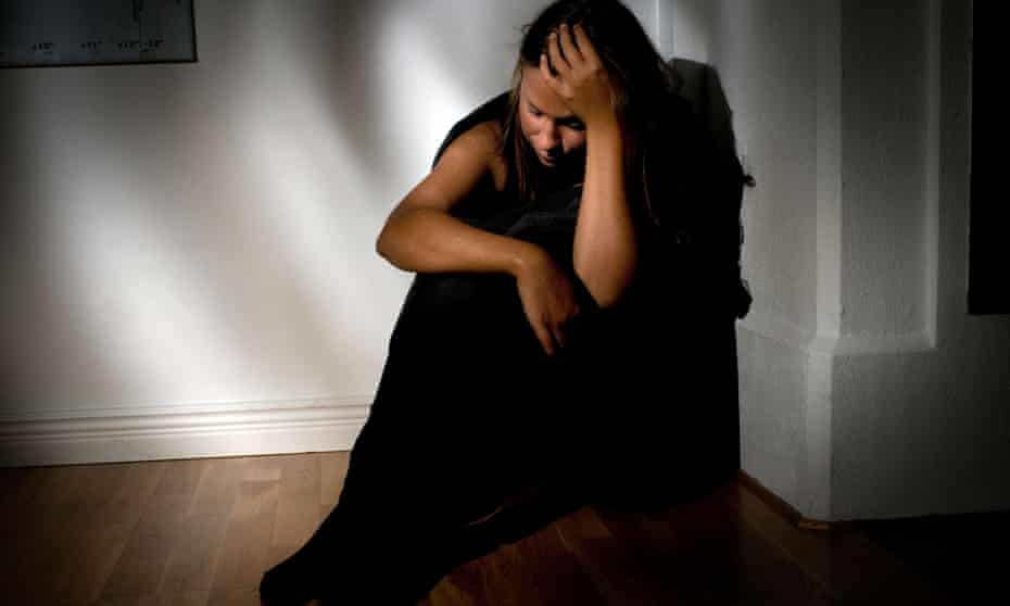 A young woman in a darkened room, head in hands, ill or depressed.