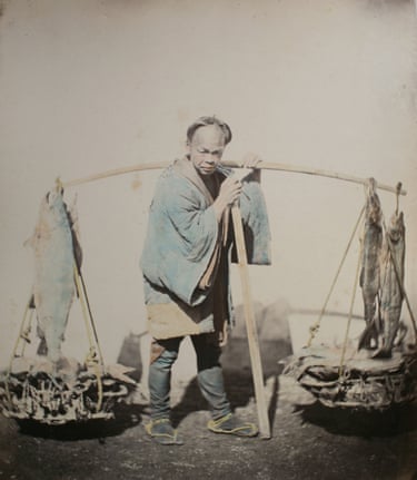 A man carries a shoulder pole with baskets of fish and whole fish hanging from ropes