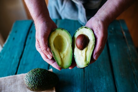 Two hands holding two cut halves of an avocado.