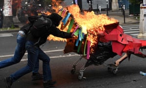 People push a burning trolley towards riot police during march in Paris