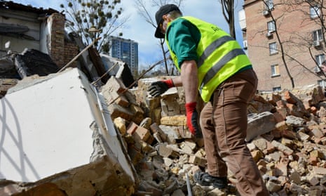 A man wearing a hi-vis vest and gloves reaches down towards a pile of rubble