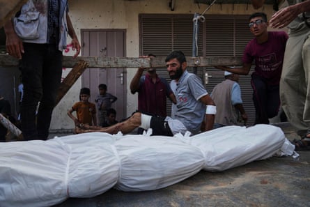 Mourners with the bodies of people in funeral shrouds.
