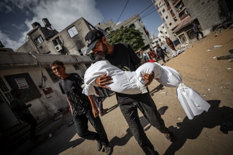 A Palestinian man carries the shrouded body of someone killed in Israeli attacks.