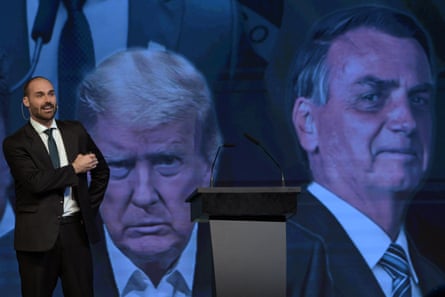 Eduardo Bolsonaro speaks on a stage in front of a giant screen bearing images of his father, Jair Bolsonaro, and Donald Trump.