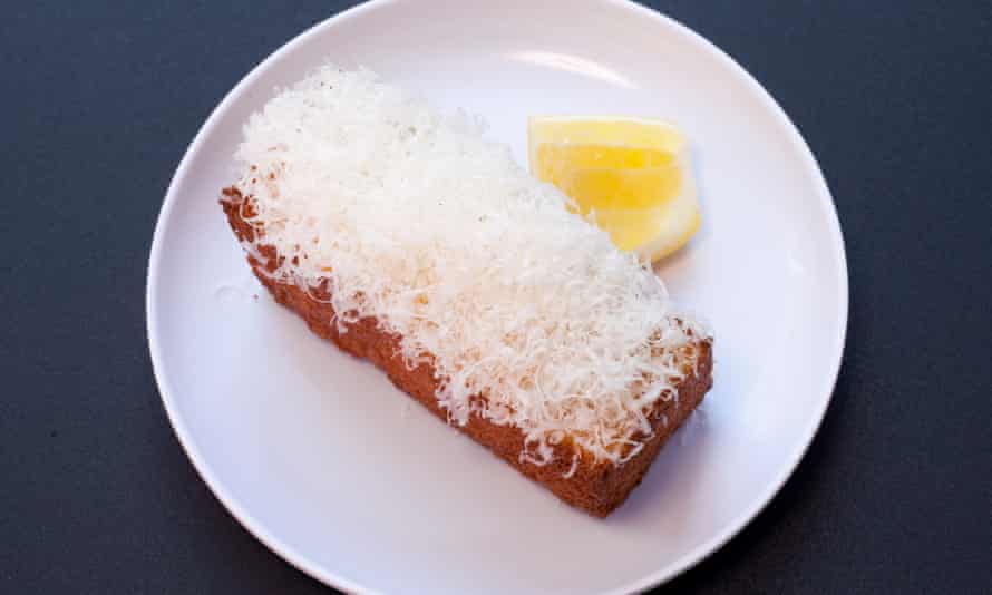 A round white plate with a rectangular 'cake' topped with white shredding and a slice of lemon next to it