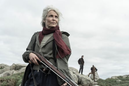 Carol gazes of into the distance while holding a weapon
