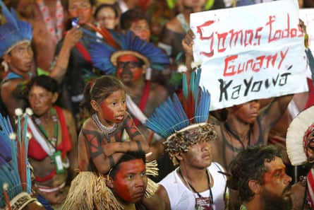 Sekelompok orang Pribumi berdiri bersama, satu di antara mereka memegang spanduk.