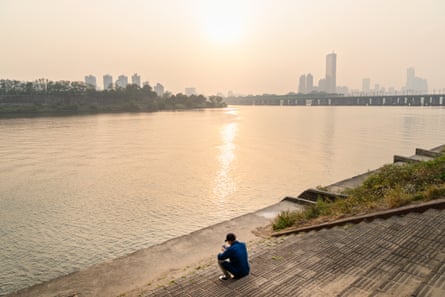 A young man having a rest at a riverside at sunset.