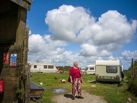 A woman stands in a field in which poultry roam and a few old caravans are parked.