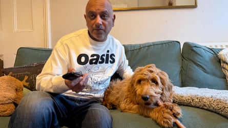 Rich Pelley and Ozzy sit on a sofa, Pelley with remote control in hand and Ozzy has a pizzle stick between his front paws.