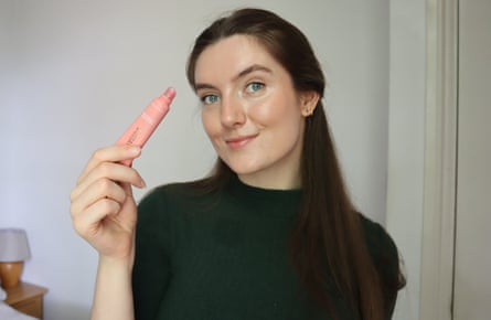 The writer holds up a pink tube of the Biossance Pro-Peptide Lip Perfector