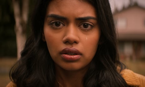 A closeup of a young Indian girl with long black hair and red lipstick looking scared into the camera, a tear running down one cheek.