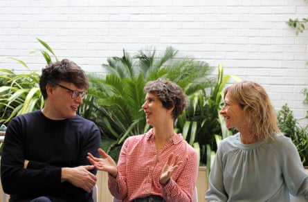Trio sat talking with plants against white wall behind