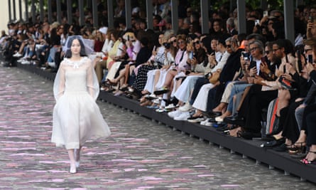 Pengantin wanita berjalan-jalan di dermaga dengan tangan di saku gaun siang gading lengan panjang selututnya