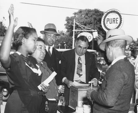 Black people approach a person at the ballot box with their ballots in hand