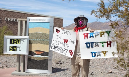 A protester stands next to a digital display of an unofficial heat reading at Furnace Creek Visitor Center during a heat wave in Death Valley National Park in Death Valley, California