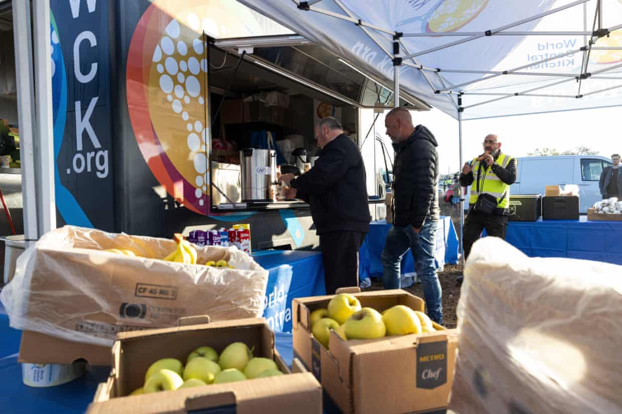 People standing at a hatch with crates of apples in the foreground.