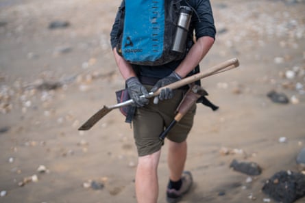 Fossil guide Martin Curtis walking away from the camera on a beach carrying a small spade and other tools