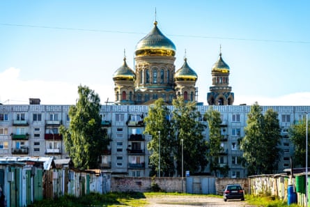 four golden onion domes of an Orthodox cathedral behind ramshaclke Soviet apartment buildings