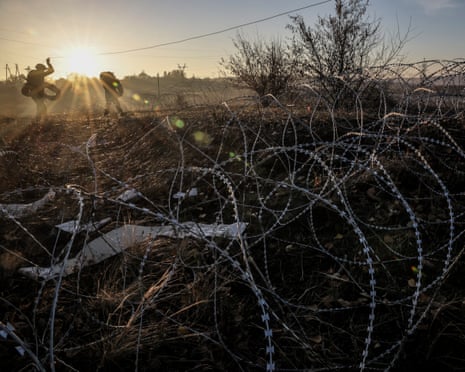 Two service personnel in silhouette near razor wire in a field