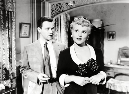 Black and white photograph shows a young man in a suit and tie holding a cigarette, talking to a young woman in a black and white dress