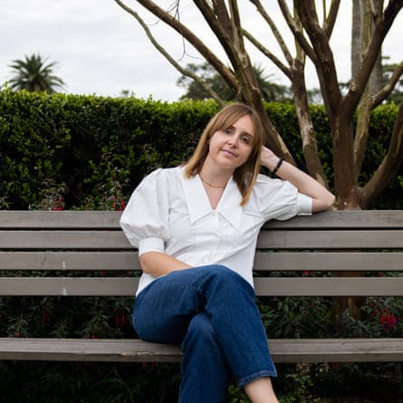 Diana Reid sitting on a park bench. She is wearing blue jeans and a white shirt and it resting her head on her arm