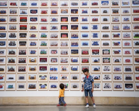 A wall covered in photographs with two children standing in front of it.