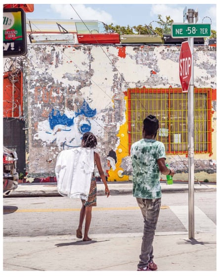 Two people crossing a road near a stop sign, walking towards a weathered shop building