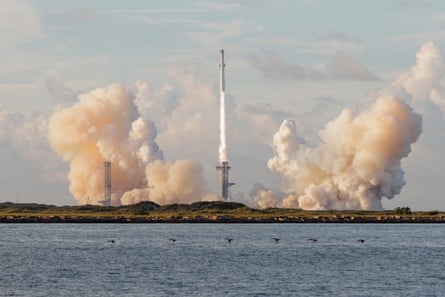 Rocket just after takeoff from launcher with smoke either side and sea in foreground