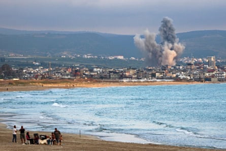 People on a beach watch as smoke rises from an Israeli strike near the southern Lebanese city of Tyre
