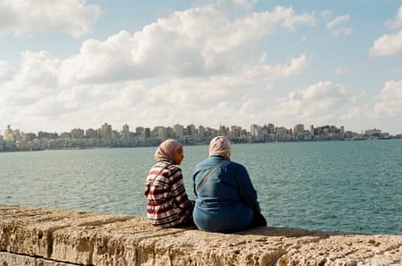Two women sit on a sea wall and chat facing the Mediterranean by the corniche in Alexandria.