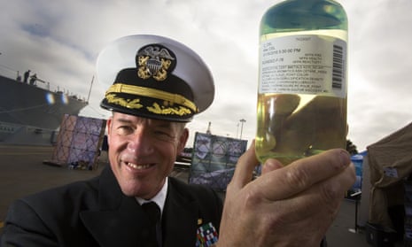 With guided missile destroyer USS Stockdale in the background, Capt Brian Weiss holds a sample of the biofuel blend.