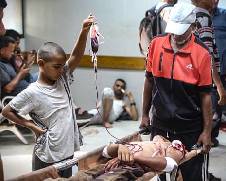 A Palestinian boy raises a pack of blood as a man who was injured at a food distribution point in Al-Tina area of Khan Younis in the southern Gaza Strip, receives medical treatment at the Nasser hospital on 19 July 2025.