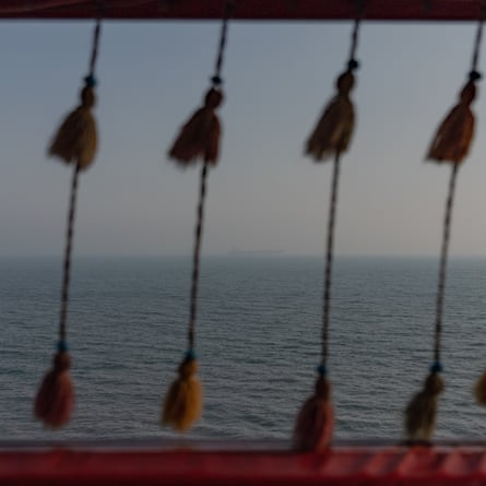 Tassels hang from a red frame overlooking a hazy sea with a distant ship