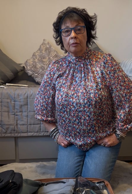 Joyce Thomas, wearing a blouse and jeans, kneeling by her suitcase next to a bed Joyce Thomas, wearing a blouse and jeans, kneeling by her suitcase next to a bed