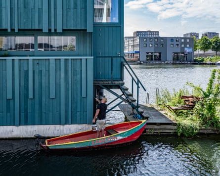 A man stands in a boat and paints his house blue