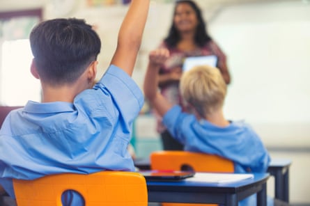 Tampilan belakang seorang siswa sekolah dasar mengangkat tangannya di ruang kelas.