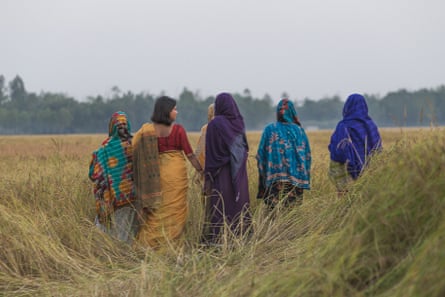 A group of Bangladeshi women stand in a field with their backs to the camera