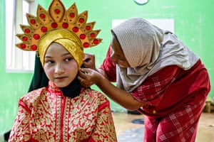 A woman prepares the golden headdress on a young dancer