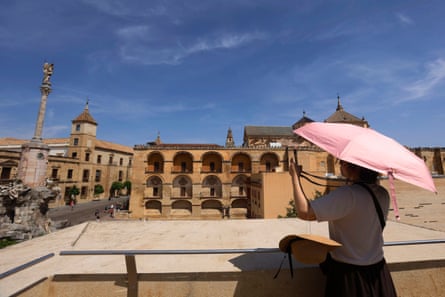 A woman holds a pink umbrella while in her other hand she uses a smartphone to take a photo of a historic building