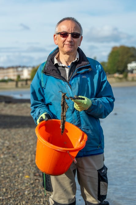 Elio Gregori holds a mucky wet wipe over a bucket on the bank of the River Thames.