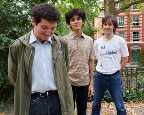 Band Pushbike's three members stand outdoors near trees and a brick building