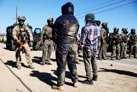 two people stand in front of a row of armed and masked federal agents