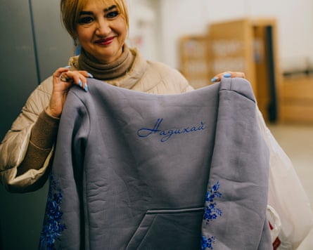 A woman with blond hair holds up a grey hooded jumper