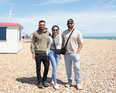 Three people standing together on a beach under a blue sky
