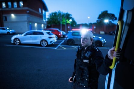 James Grundy stands beside a vehicle in the early morning light with cars behind him in a still-dark car park. He is in his early 40s with a shaven head and short beard.